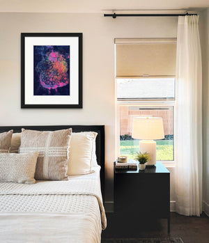 An abstract screen print by Naima Lowe in dark blues, purples, hot pink, orange and yellow shown framed in a neutral colored bedroom scene. 