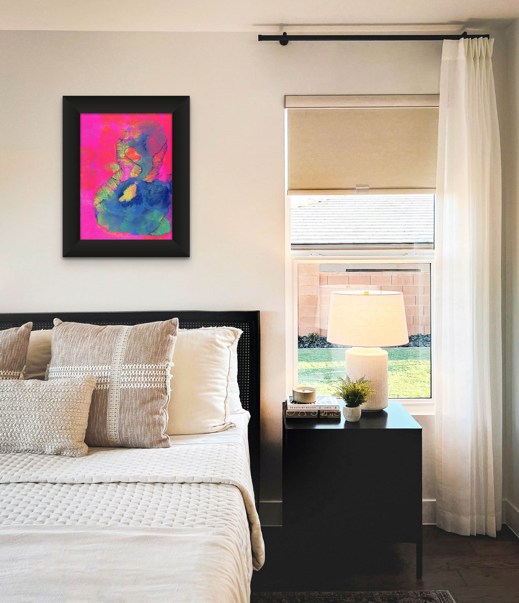 A screen print by Naima Lowe hot pinks, blues, oranges and yellows shown framed in a neutral colored bedroom scene. 