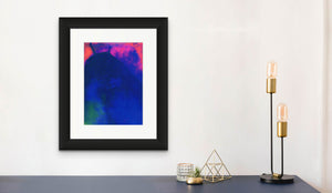 An abstract screen print by Naima Lowe in dark blues, purples, pinks and oranges shown framed in a neutral colored domestic space