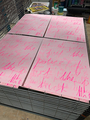 A stack of pink prints on light pink paper, with dark pink cursive handwriting bearing the phrase "Fuck the Police" many times overlapping in different sizes. In the background is a printing studio. 